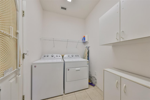 clothes washing area with cabinets, light tile patterned floors, and washer and clothes dryer