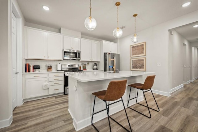 kitchen featuring white cabinetry, appliances with stainless steel finishes, an island with sink, and hanging light fixtures