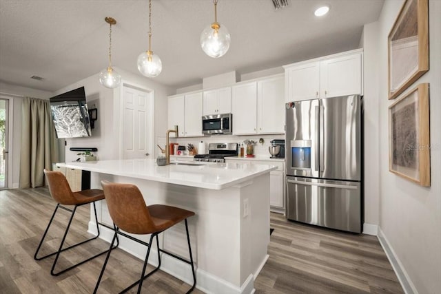 kitchen with sink, white cabinetry, decorative light fixtures, stainless steel appliances, and a kitchen island with sink