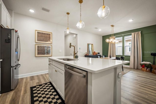 kitchen with pendant lighting, sink, white cabinetry, stainless steel appliances, and an island with sink