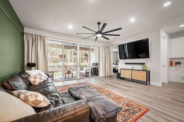 living room with ceiling fan, a textured ceiling, and light hardwood / wood-style floors