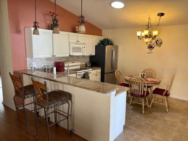 kitchen with light stone counters, kitchen peninsula, pendant lighting, white appliances, and white cabinets