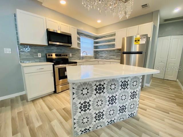 1829 10th St N, Saint Petersburg, FL 33704 - kitchen with appliances with stainless steel finishes, white cabinetry, decorative backsplash, a center island, and light hardwood / wood-style flooring