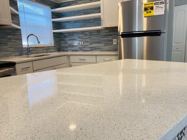 1829 10th St N, Saint Petersburg, FL 33704 - kitchen with white cabinetry, stainless steel fridge, sink, and backsplash
