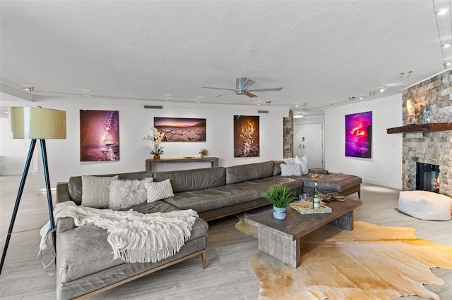 living room with a fireplace, ornamental molding, ceiling fan, light hardwood / wood-style floors, and a textured ceiling