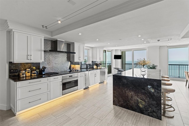 kitchen featuring appliances with stainless steel finishes, a center island, wall chimney range hood, and white cabinets