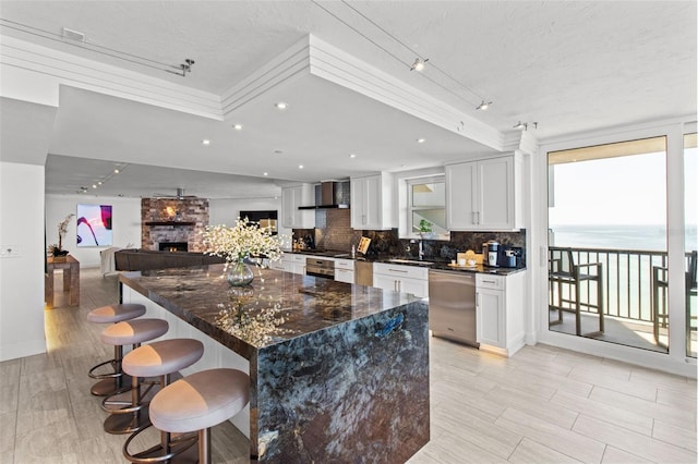 kitchen with white cabinetry, a water view, dishwasher, decorative backsplash, and wall chimney range hood