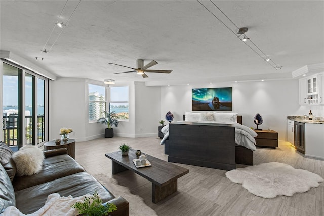 living room with ceiling fan, indoor bar, a textured ceiling, and light wood-type flooring