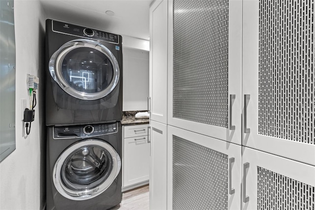 clothes washing area featuring cabinets, light hardwood / wood-style flooring, and stacked washer and clothes dryer