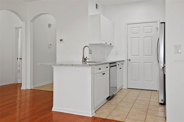 kitchen with sink, white cabinetry, stainless steel appliances, light stone countertops, and kitchen peninsula