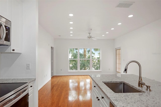 kitchen with white cabinetry, sink, light stone counters, stainless steel appliances, and light hardwood / wood-style flooring