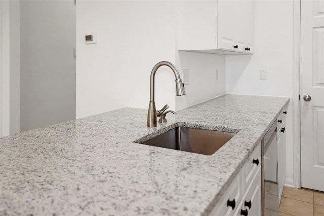 kitchen featuring dishwasher, white cabinetry, sink, light tile patterned floors, and light stone countertops