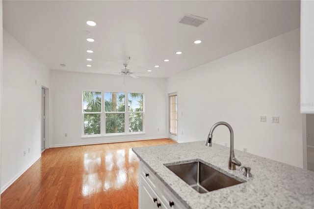 kitchen featuring sink, light stone counters, white cabinetry, light hardwood / wood-style flooring, and ceiling fan