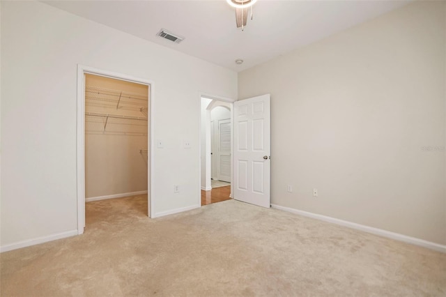 unfurnished bedroom featuring a walk in closet, light carpet, and a closet