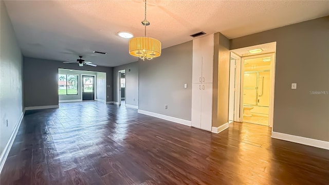 spare room featuring dark wood-type flooring, ceiling fan with notable chandelier, and a textured ceiling