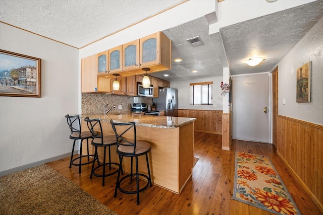 kitchen featuring appliances with stainless steel finishes, a kitchen bar, kitchen peninsula, and wood walls