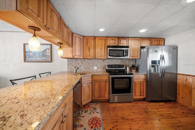 kitchen featuring a kitchen bar, sink, decorative light fixtures, appliances with stainless steel finishes, and light stone countertops