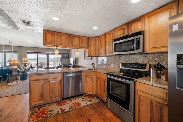 kitchen featuring light stone counters, stainless steel appliances, light hardwood / wood-style floors, and decorative backsplash