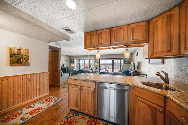 kitchen with sink, dishwasher, light stone counters, light wood-type flooring, and wood walls