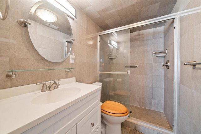 bathroom featuring vanity, a shower with shower door, tile walls, and toilet