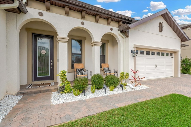 entrance to property featuring stucco siding, decorative driveway, and a garage