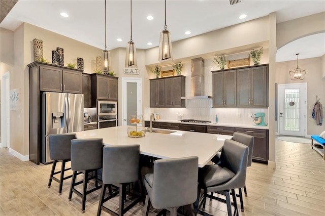 kitchen featuring stainless steel appliances, a sink, decorative light fixtures, dark brown cabinetry, and wall chimney exhaust hood