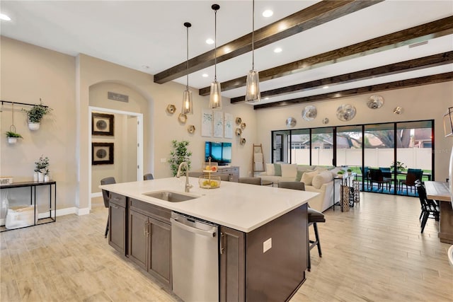 kitchen with hanging light fixtures, an island with sink, a sink, light countertops, and dishwasher