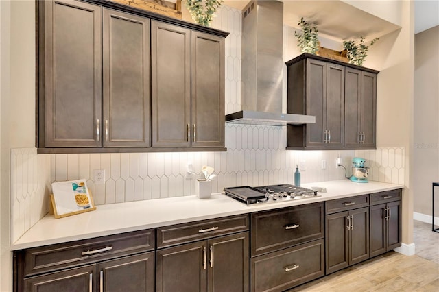 kitchen with light countertops, stainless steel gas stovetop, backsplash, and wall chimney range hood