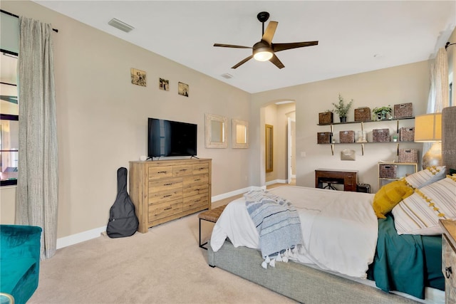 bedroom featuring light carpet, baseboards, visible vents, arched walkways, and ceiling fan