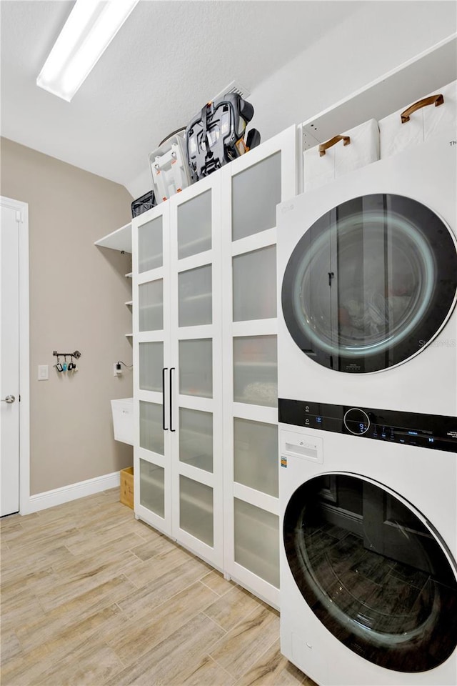 laundry area featuring baseboards, stacked washer and dryer, laundry area, and light wood-type flooring