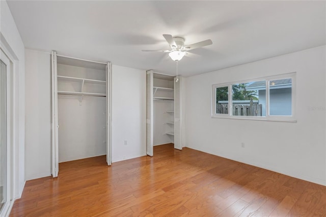 unfurnished bedroom featuring baseboards, a ceiling fan, two closets, and wood finished floors