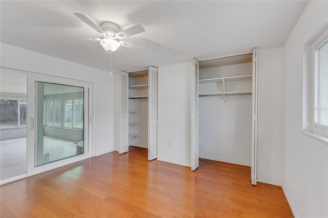 unfurnished bedroom with multiple closets, multiple windows, light wood-style floors, and a ceiling fan