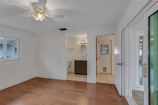 interior space with visible vents, light wood-style floors, connected bathroom, a sink, and baseboards