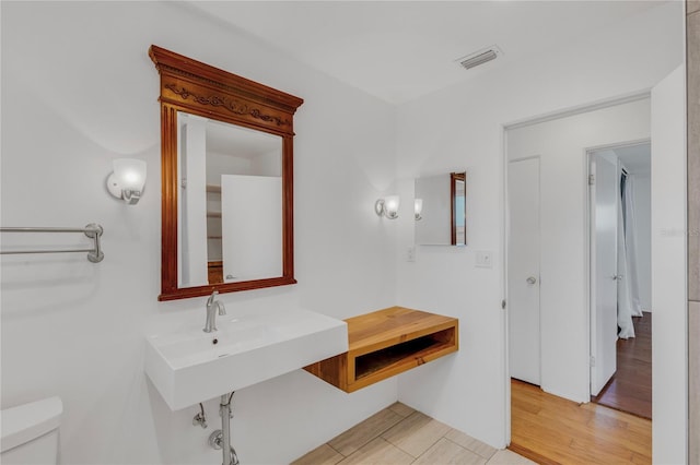 bathroom featuring visible vents, a sink, toilet, and wood finished floors