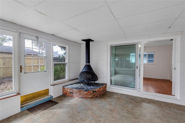 unfurnished sunroom featuring a paneled ceiling and a wood stove