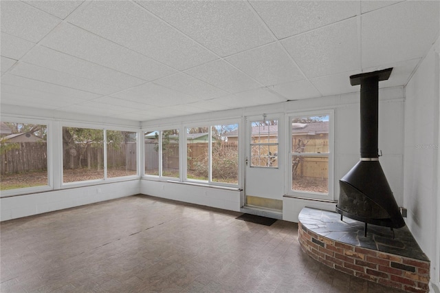 unfurnished sunroom featuring a wood stove and a drop ceiling