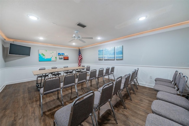 cinema with dark wood finished floors, crown molding, visible vents, a ceiling fan, and wainscoting