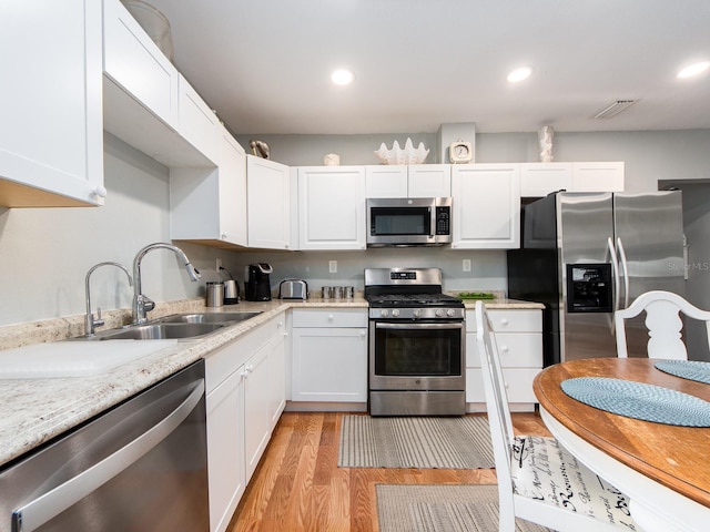 kitchen featuring light wood-type flooring, stainless steel appliances, light stone countertops, white cabinets, and sink