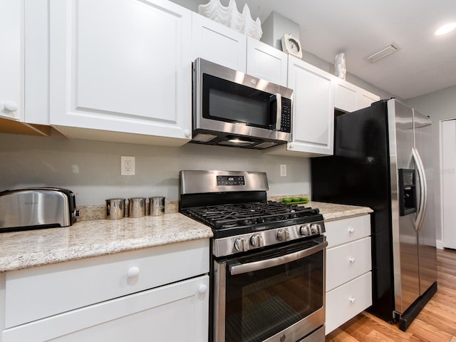 kitchen with white cabinets, light hardwood / wood-style floors, appliances with stainless steel finishes, and light stone counters