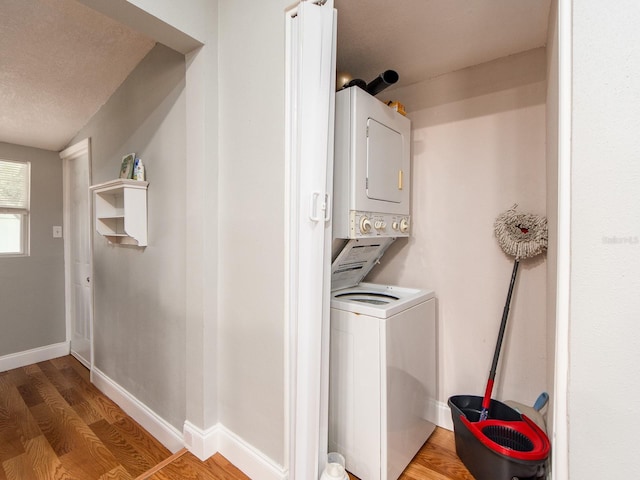 laundry room with wood-type flooring, stacked washer and clothes dryer, and a textured ceiling