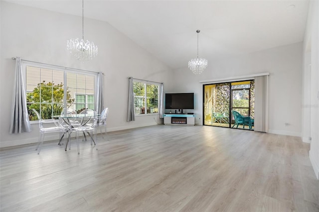 unfurnished living room with an inviting chandelier, high vaulted ceiling, and light wood-type flooring