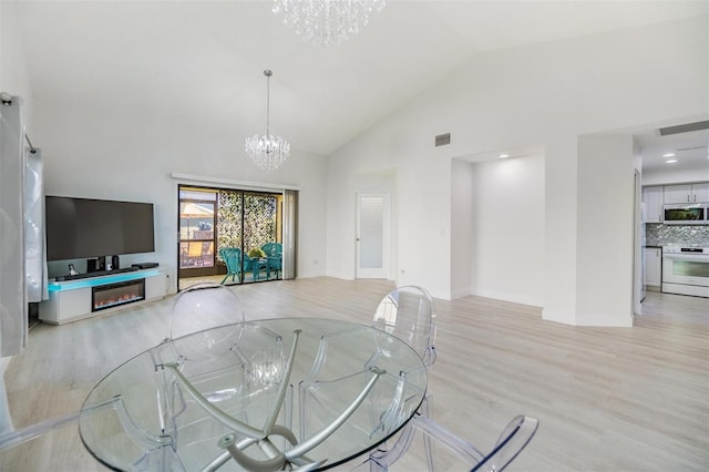 living room with a notable chandelier, light hardwood / wood-style floors, and high vaulted ceiling