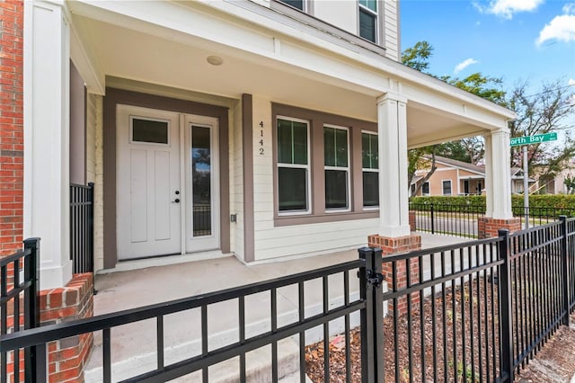 doorway to property with covered porch, brick siding, and fence