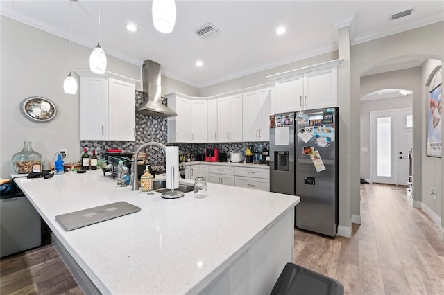 kitchen with arched walkways, crown molding, backsplash, wall chimney range hood, and stainless steel fridge