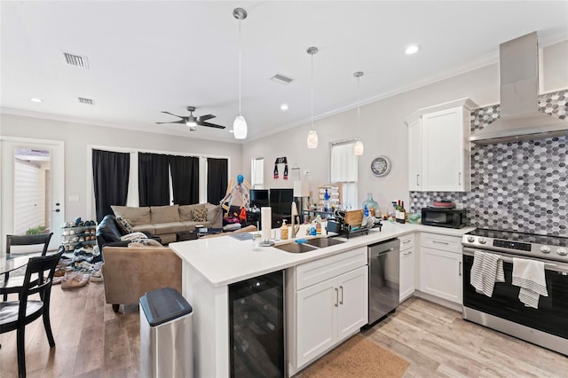 kitchen featuring wine cooler, appliances with stainless steel finishes, a peninsula, wall chimney range hood, and a sink