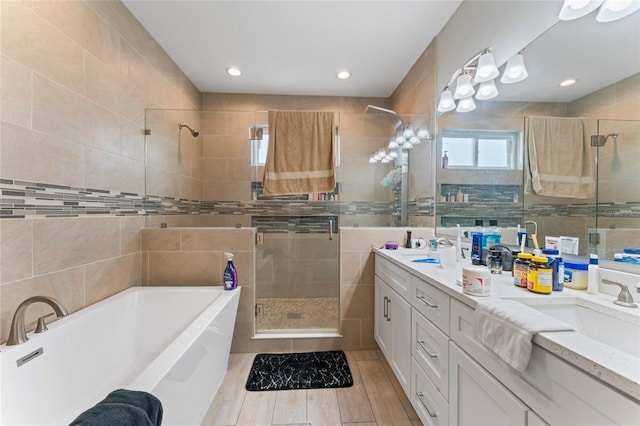 full bathroom featuring double vanity, a stall shower, tile walls, a freestanding tub, and a sink