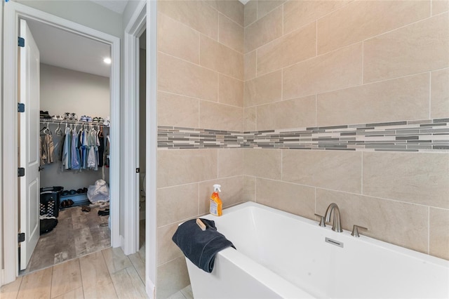 full bathroom featuring a spacious closet, wood finished floors, a bathing tub, and tile walls