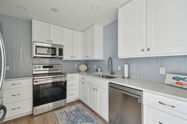 kitchen with stainless steel appliances, a sink, decorative backsplash, and wood finished floors