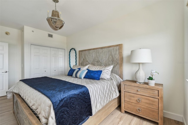 bedroom with light wood finished floors, a closet, visible vents, and baseboards