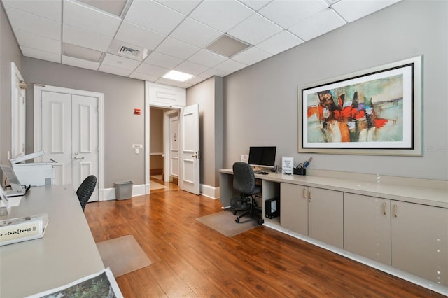 office featuring baseboards, visible vents, a drop ceiling, and wood finished floors